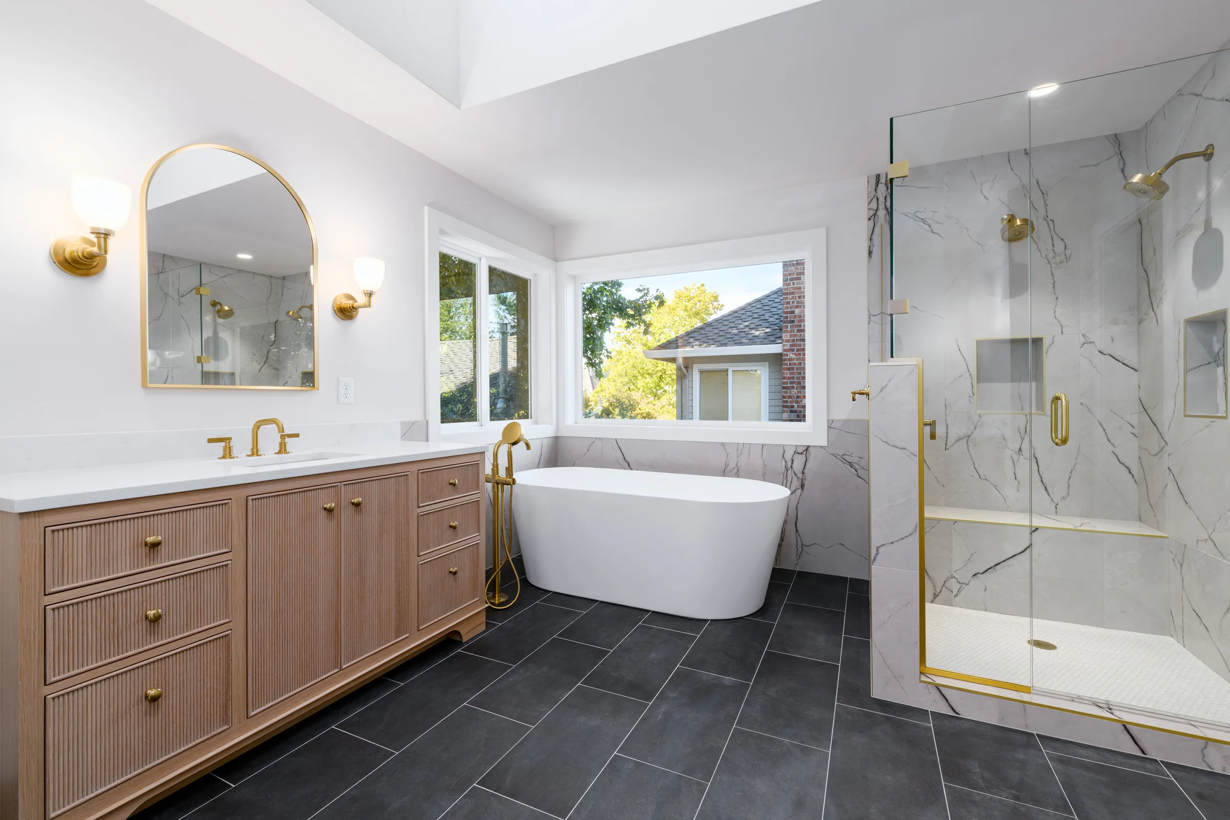 Bathroom remodel with a freestanding tub, brass fixtures, and arched mirror