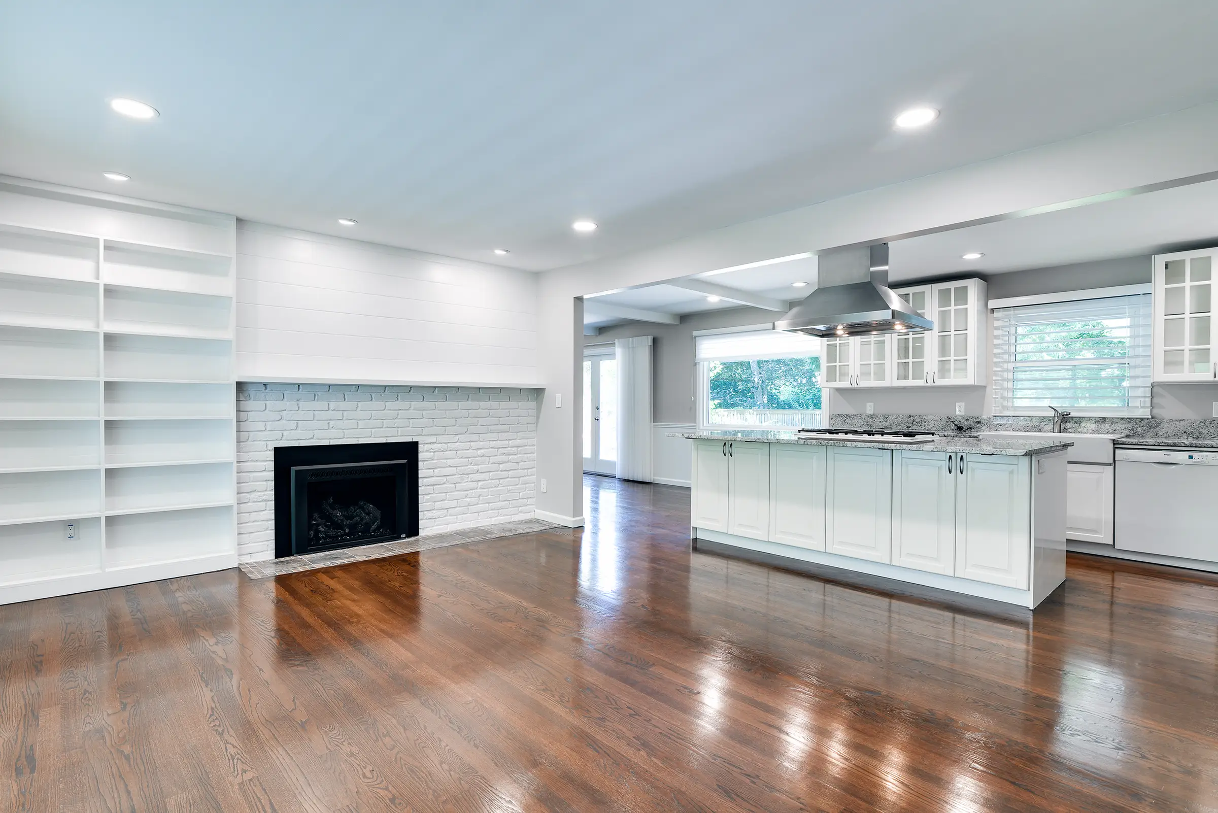 Living room with a painted brick fireplace and built-in shelving, open to the kitchen