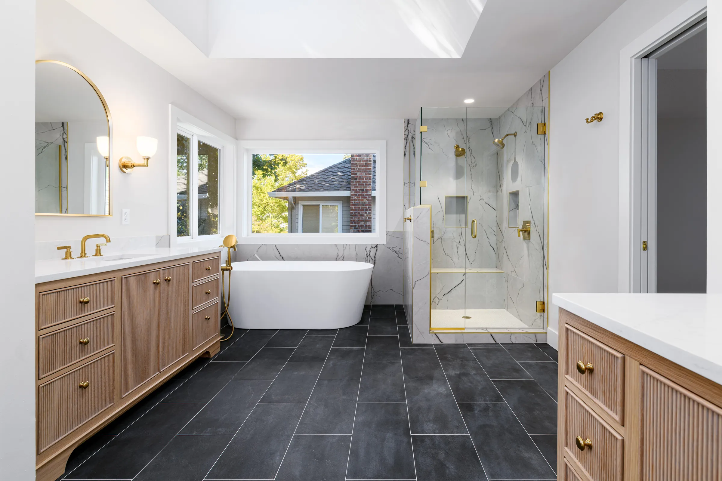 Remodeled bathroom with a freestanding tub, glass shower, and white-oak double vanity