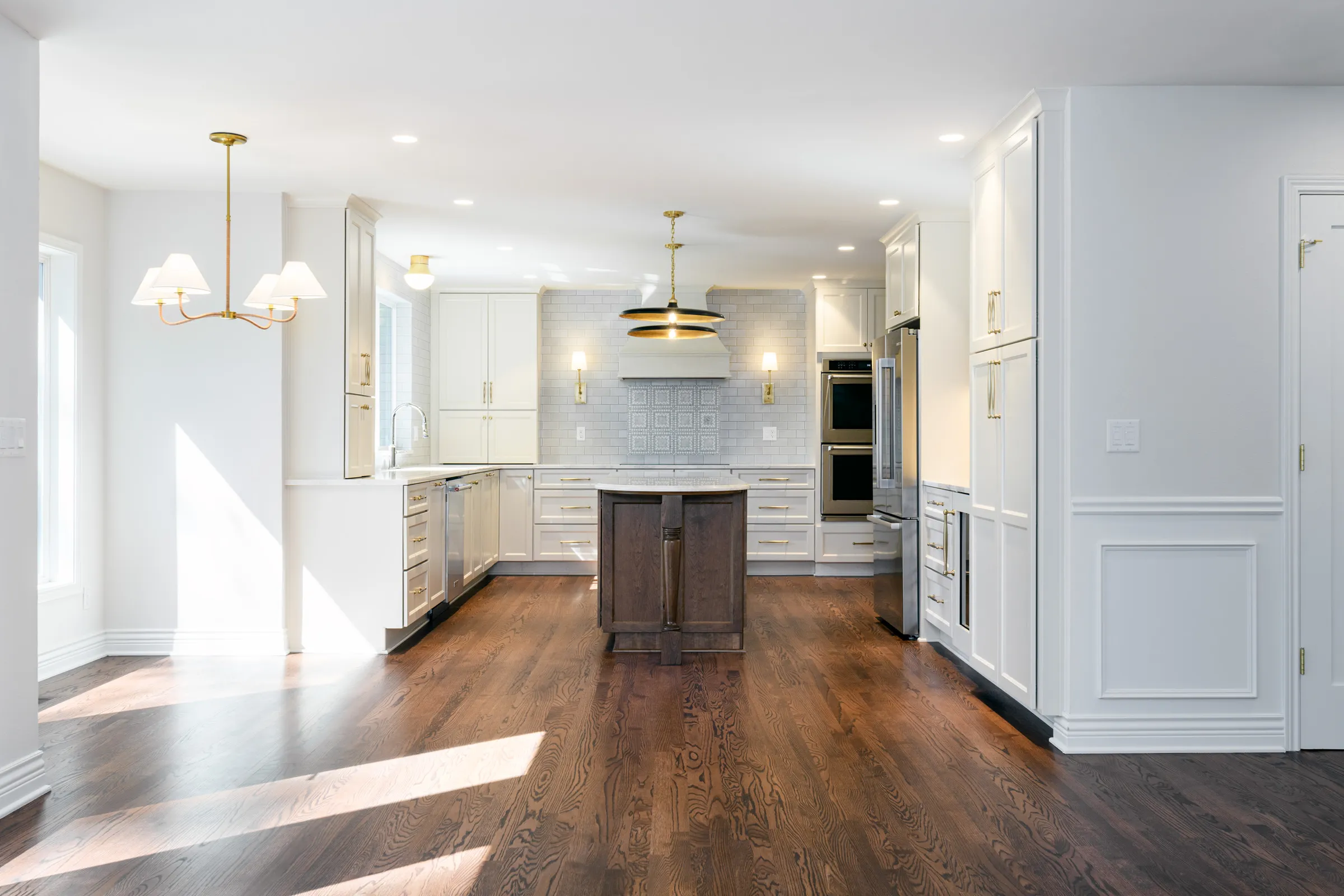 Open white kitchen with a wood-topped island and brass chandelier after a Lake Oswego remodel