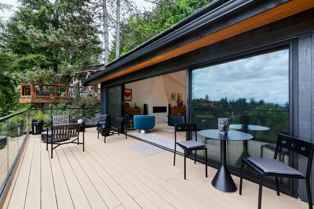 Covered second-story deck lounge with an open glass wall and forest view after the West Hills expansion